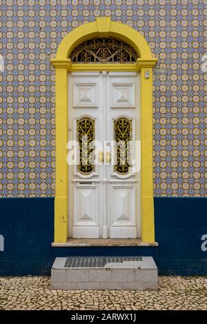 Portugal, Fassade eines Hauses mit typischen Keramikazulejos-Fliesen und einer verzierten Holztür in Weiß und Gelb Stockfoto