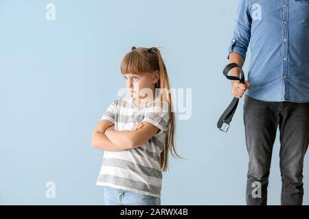 Mann bedroht seine kleine Tochter vor Farbhintergrund. Konzept der körperlichen Bestrafung Stockfoto