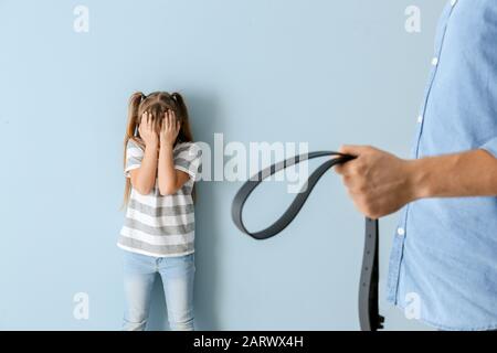 Mann bedroht seine kleine Tochter vor Farbhintergrund. Konzept der körperlichen Bestrafung Stockfoto