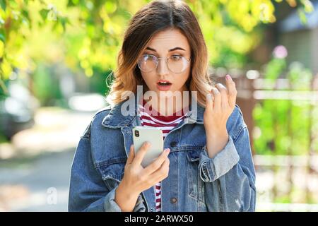 Überraschte junge Frau mit Handy im Freien Stockfoto