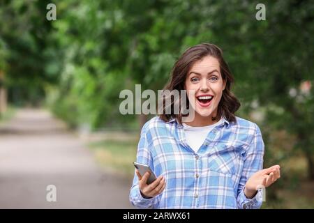 Überraschte junge Frau mit Handy im Freien Stockfoto