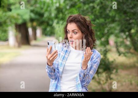 Überraschte junge Frau mit Handy im Freien Stockfoto