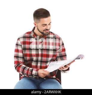 Gutaussehender Mann mit Zeitung, die vor weißem Hintergrund auf dem Stuhl sitzt Stockfoto