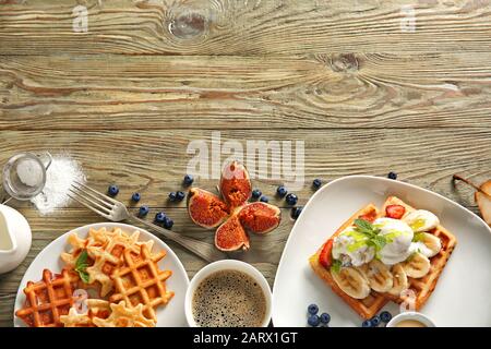 Teller mit leckeren Waffeln, Eis und Kaffee auf Holztisch Stockfoto