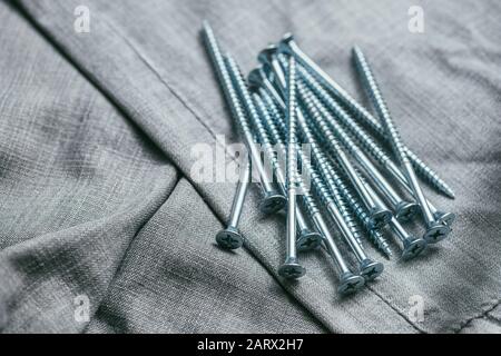 Eine Handvoll metallischer selbstschneiderschrauben liegt vor dem Hintergrund eines alten Denim-Stoffes. Makroaufnahme mit selektivem Fokus und flachem Freiheitsgrad Stockfoto