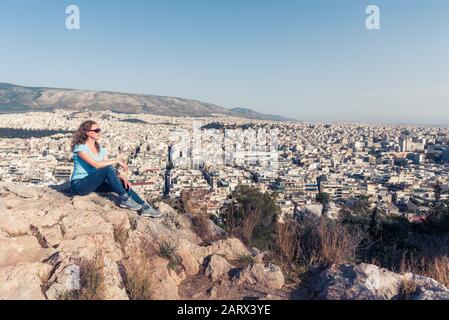 Junge hübsche Frau blickt auf die Stadt Athen, Griechenland. Schöner Erwachsenen-Tourist entspannt mit Blick auf Athen im Sommer. Attraktive Person steht im Hintergrund Stockfoto