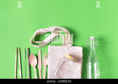 Umweltfreundliches Einweggeschirr aus Bambusholz und Glasmauerbecher und Flasche auf mintgrünem Hintergrund Draufsicht. Kopierbereich.
