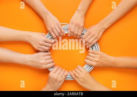 Weibliche Hände mit elektrischem Kabel auf Farbhintergrund Stockfoto