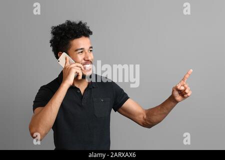 Porträt eines afroamerikanischen Mannes, der mit dem Handy spricht, auf grauem Hintergrund Stockfoto
