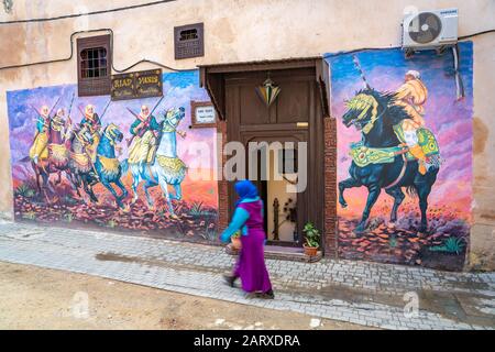 Meknes, Marokko - Eine Frau, die in der alten Medina ein buntes Wandgemälde spaziert Stockfoto