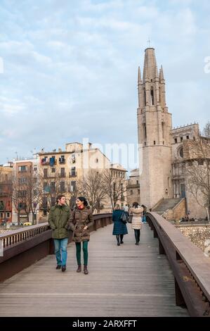Menschen, die auf einer Brücke über den Fluss Onyar spazieren, Die Häuser am Fluss Onyar mit der Kirche Sant Felix im Hintergrund, Girona, Katalonien, Spanien Stockfoto