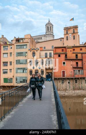 Menschen, die auf einer Brücke über den Fluss Onyar spazieren, Die Häuser am Fluss Onyar mit der Kathedrale im Hintergrund, Girona, Katalonien, Spanien Stockfoto