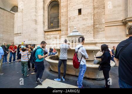 Touristen trinken und füllen ihre Flaschen mit Wasser im Innenhof des hinteren Tores des Petersdoms und des Vatikanischen Museums. Stockfoto