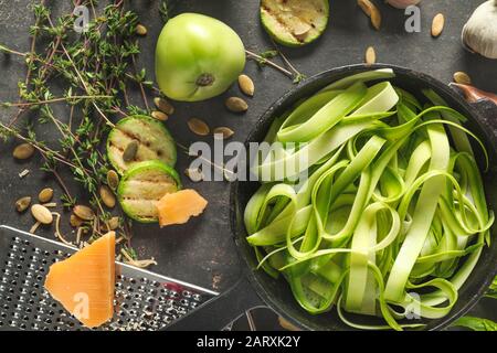 Bratpfanne mit leckeren Zucchini-Pasta und Zutaten auf dunklem Hintergrund Stockfoto