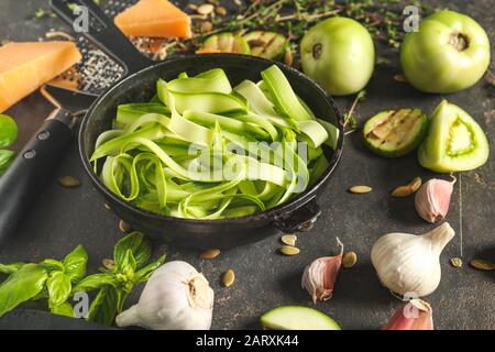 Bratpfanne mit leckeren Zucchini-Pasta und Zutaten auf dunklem Hintergrund Stockfoto