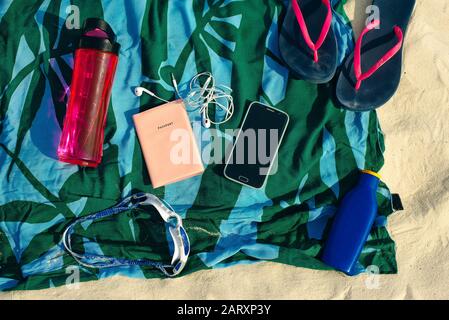Urlaub und Sommerferien Konzept - Flip-Flops, Handtuch, Kappe, Flaschenwasser und Flasche Sonnenschutzöl am Strand Stockfoto