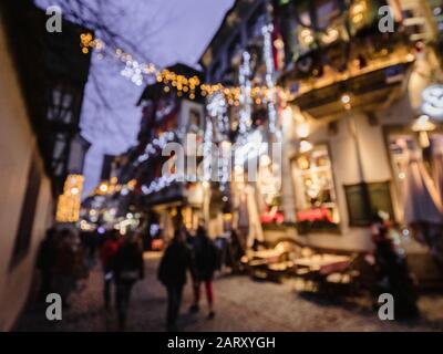 Entschärfte weite Aussicht auf das Restaurant Le Gruber in der berühmten Fußgängerzone mit Touristen Menschen Silhouetten, die die jährlichen Weihnachtsmarktdekorationen entdecken Stockfoto