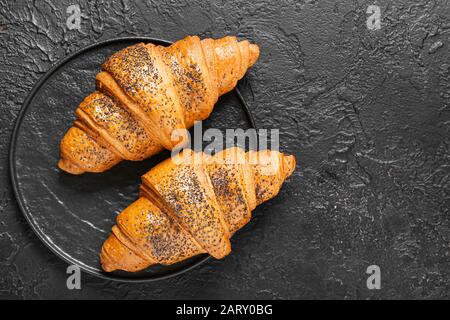 Teller mit leckeren Croissants auf dunklem Hintergrund Stockfoto