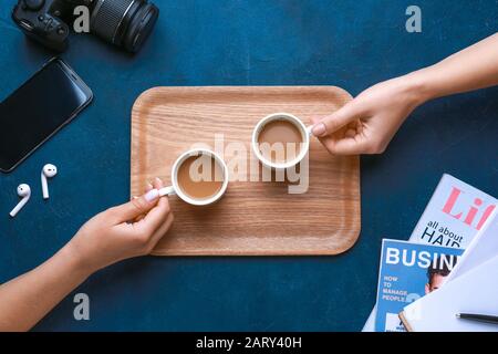 Weibliche Hände mit Kaffeetassen auf farbigem Hintergrund Stockfoto