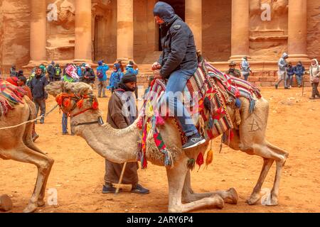 Petra, Jordanien - 4. Januar 2020: Nahaufnahme eines Beduinen, während er einen Touristen von seinem Dromedarkamel vor Petras beliebtester historischer Stätte, dem, lässt Stockfoto