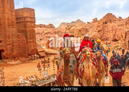 Petra, Jordanien - 4. Januar 2020: Beduinen und Touristen fahren in den monumentalen Petra, UNESCO-Weltkulturerbe, einer historischen und archäologischen Stätte, mit verdrossener Kamele Stockfoto