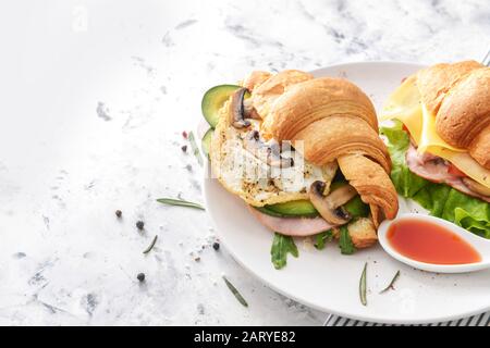 Teller mit leckeren Croissant Sandwiches und Soße auf weißem Hintergrund Stockfoto