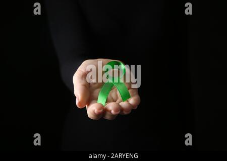 Weibliche Hand mit grünem Band auf dunklem Hintergrund. Konzept für das Krebsbewusstsein Stockfoto