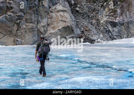 Profi-Eiskletterer spazieren auf dem Gletscher. Wandern auf dem Eis. Grauer Felsenberg im Hintergrund. Der Mann trägt eine komplette Ausstattung und einen Helm. Stockfoto