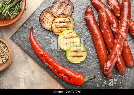 Leckere Grillwürste mit Gemüse auf Schieferplatte Stockfoto