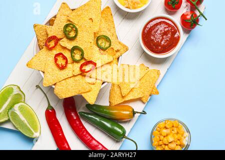 Brett mit leckeren Nachos, Soßen und Chili Pfeffer auf Farbhintergrund Stockfoto