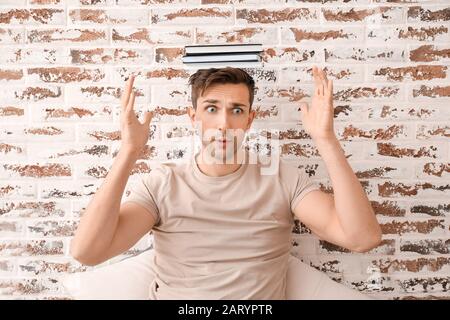 Besorgter junger Mann mit Büchern über Backstein-Hintergrund Stockfoto