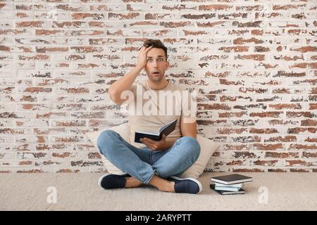 Schockierter junger Mann mit Büchern in der Nähe der Ziegelmauer Stockfoto