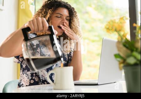 Müde Frau Gießen Kaffee von Laptop Stockfoto