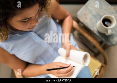 Frau sitzt auf einem Stuhl und schreibt in einem Notizbuch Stockfoto