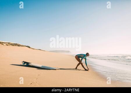 Frau trägt Neoprenanzug Stretching am Strand Stockfoto