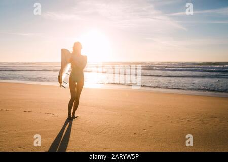 Frau hält Surfbrett gegen Sonnenlicht am Strand Stockfoto