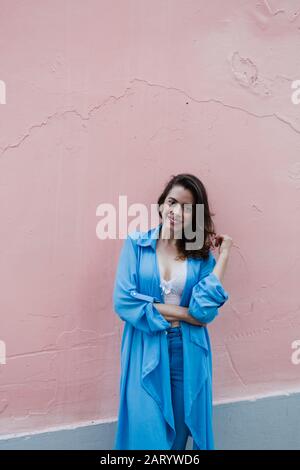 Lächelnde Frau trägt blau durch rosa Wand Stockfoto