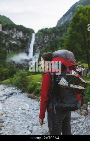 Frau trägt Rucksack mit Wasserfall in der Ferne Stockfoto