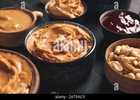 Schalen mit leckerem Erdnussbutter und Marmelade auf dunklem Tisch Stockfoto