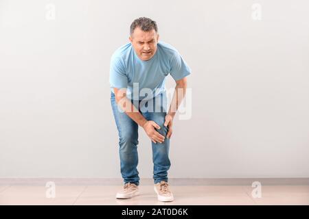 Reifer Mann, der an Schmerzen im Knie in der Nähe der Wand leidet Stockfoto