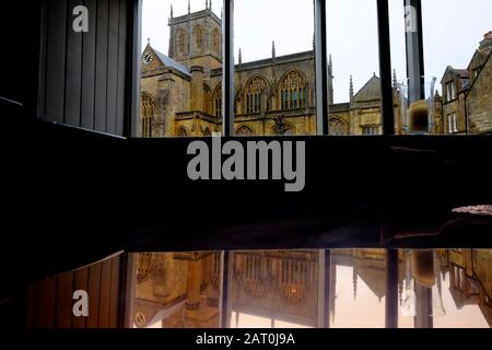 Sherborne Abbey durch Pub-Fenster, das sich in kupferbeschlagenen Tischen widerspiegelt Stockfoto