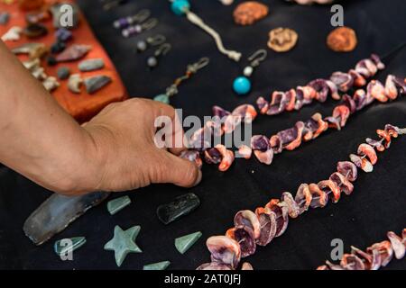 Nahaufnahme der Hand des Mannes, die eine Halskette vom Stand eines Verkäufers wählt. Bauernmarkt vor Ort machte Schmuck mit Schmuck auf schwarzem Samttuch Stockfoto