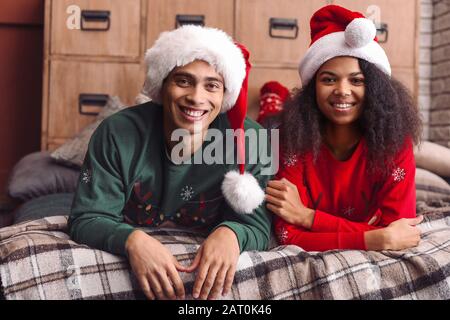 Glückliches afroamerikanisches Paar in Santa Hüten zu Hause am Weihnachtabend Stockfoto