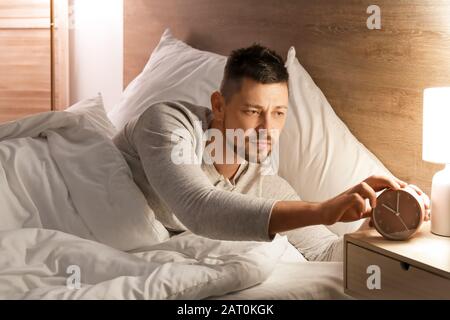 Gutaussehender Mann, der nachts im Bett liegt und einen Alarm auslöst Stockfoto