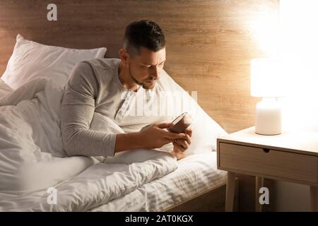 Gutaussehender Mann, der nachts im Bett liegt und einen Alarm auslöst Stockfoto