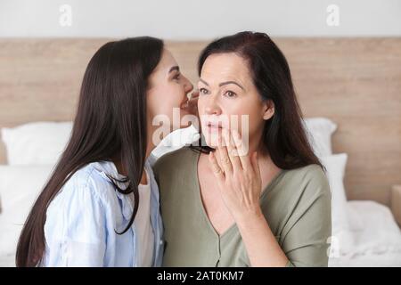 Erwachsene Tochter, die ihrer Mutter zu Hause geheim erzählt Stockfoto