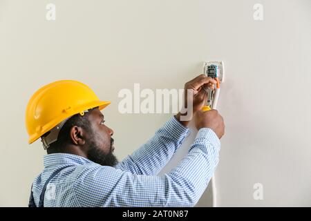 Afroamerikanischer Elektriker installiert Schalter im Raum Stockfoto