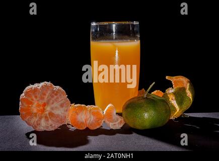 Orangen Tangerin und Glas, Zitrusreticula. Auf dem Tisch mit schwarzem Hintergrund und Hintergrundbeleuchtung Stillleben .Mandarinsorte Orange enthält pomelo und c V Stockfoto