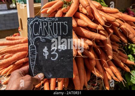 Handschriftlich geschriebenes Schild mit dem Preis für leuchtend orangefarbene Karotten auf dem Bauernmarkt. Echte, echte Lebensmittel aus dem Land, zum Verkauf. Stockfoto