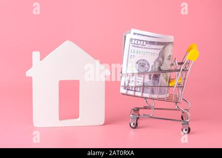 Abbildung von Haus und Geld im Warenkorb auf Farbhintergrund. Konzept des Kaufs von Immobilien Stockfoto